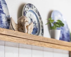 Eine Cherub-Figur aus Keramik steht auf einem Holzregal neben blauen und weißen Deko-Tellern und kleinen Topfpflanzen und schafft eine gemütliche und dekorative Atmosphäre.