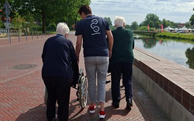Eine Mitarbeiterin der Tagespflege mit Plan begleitet zwei Seniorinnen bei einem Spaziergang am Berkelufer in Stadtlohn